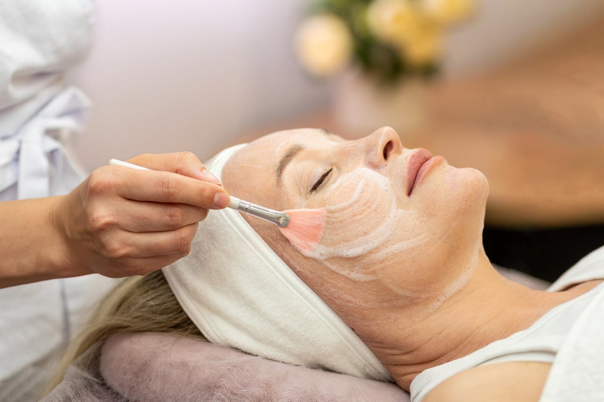 Cerca de una esteticista aplicando mascarilla facial durante un tratamiento profesional de belleza para una piel saludable