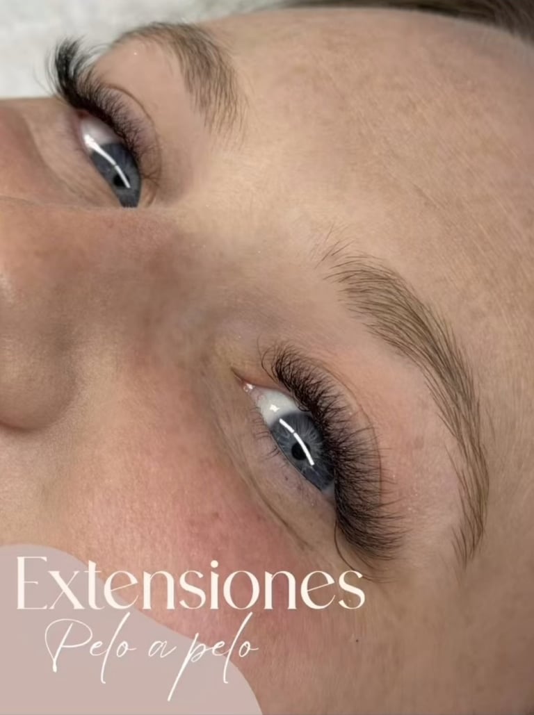 Close-up of eyelash extensions with dark makeup and defined eyebrows on a models face, labeled Extensiones Pelo a pelo