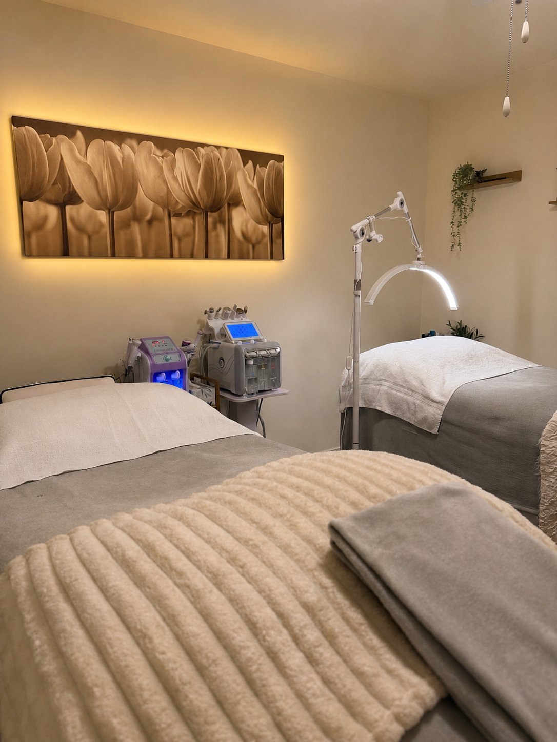 Modern spa treatment room with two massage beds, medical equipment, and a golden tulip wall art illuminated by warm lighting