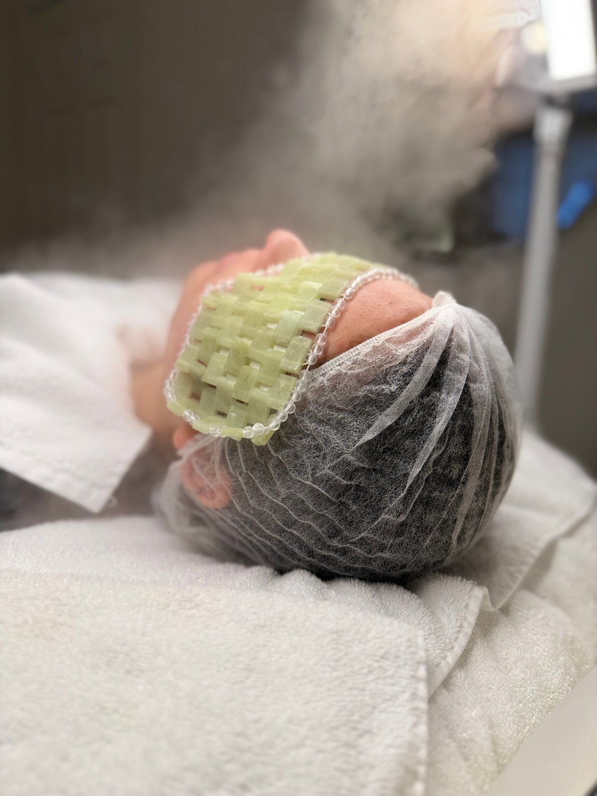 Newborn babys foot wrapped in gauze with a small green medical patch applied, resting on white cloth